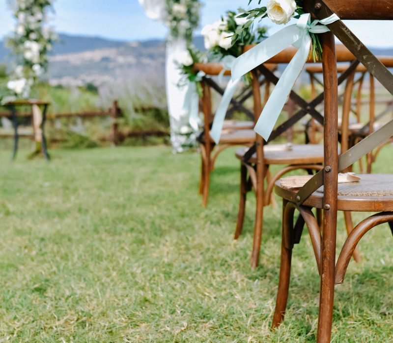 Brown chiavari chairs decorated with white eustomas on the grass and the decorated wedding archway on the background