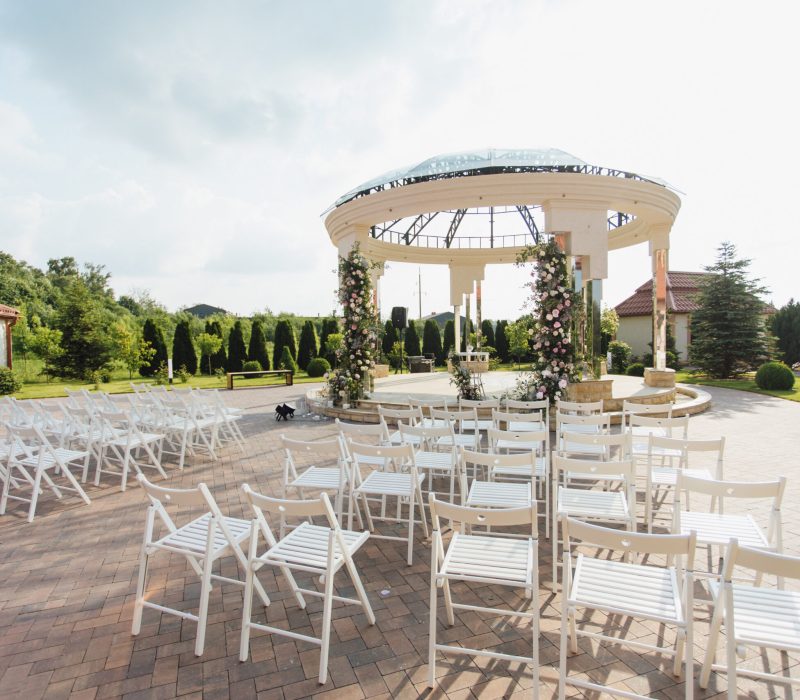 View of white guest chairs and decorated ceremonial archway open air on the sunny day